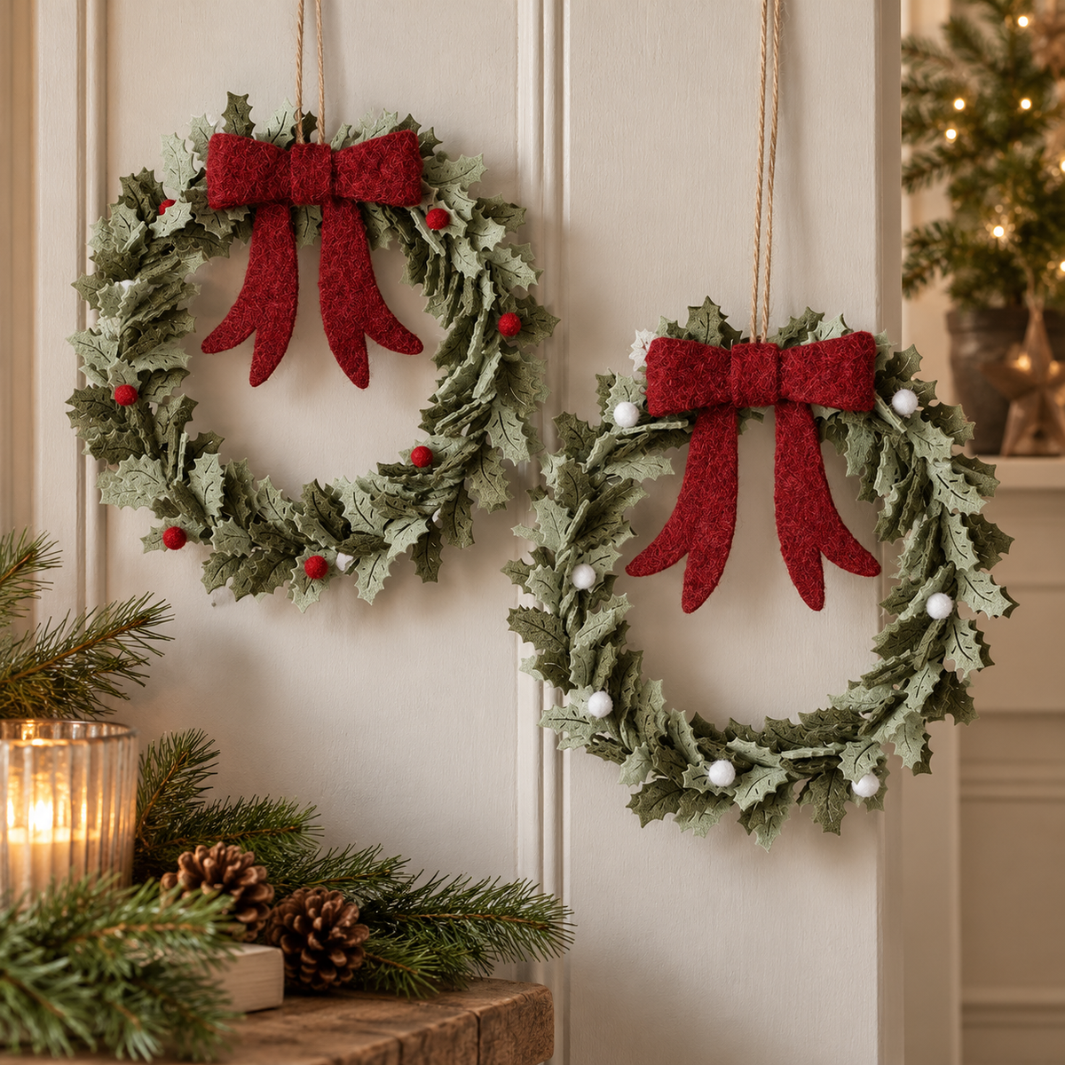 Two felt holly Christmas wreaths with red bows and red or white berries hanging on a cream wall