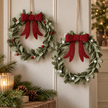 Two felt holly Christmas wreaths with red bows and red or white berries hanging on a cream wall