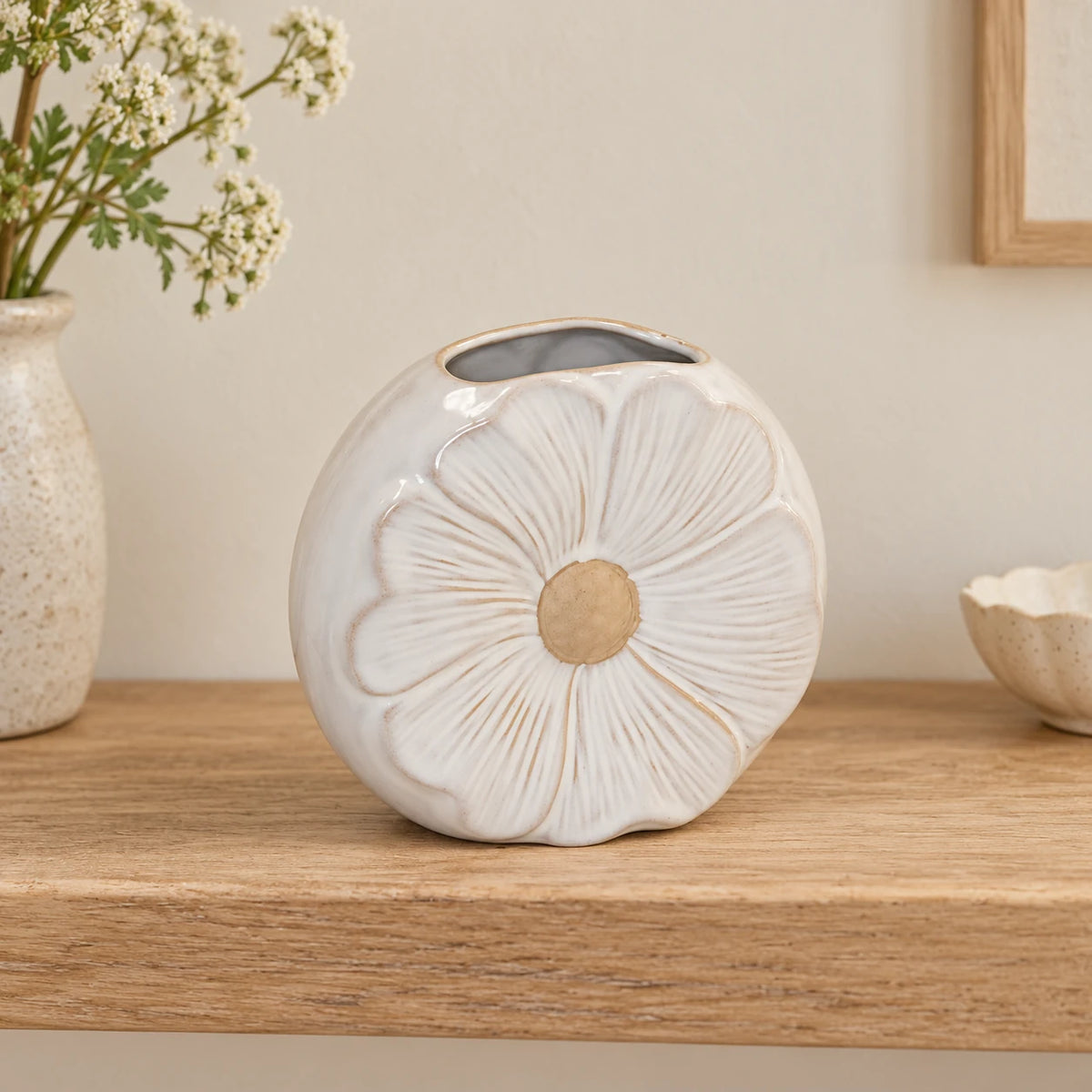 Empty flower detailed small vase on a pale oak shelf against a cream wall