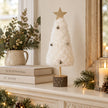 White fluffy Christmas tree with bells on a cream mantel.