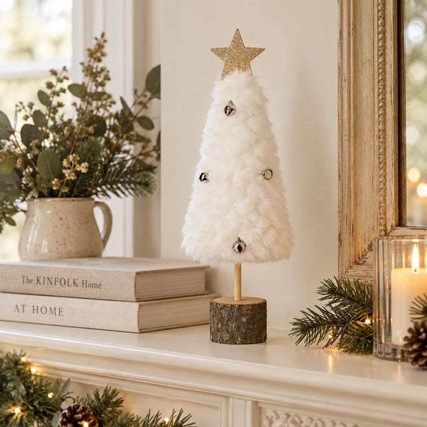 White fluffy Christmas tree with bells on a cream mantel.
