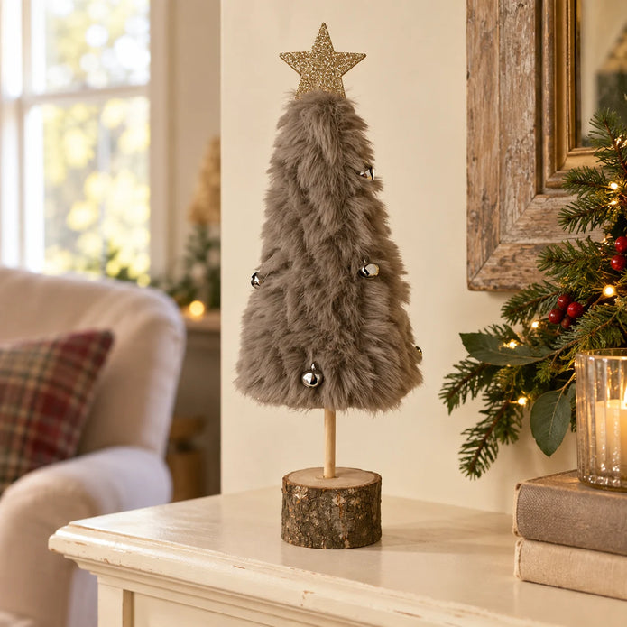 Grey fluffy Christmas tree with bells on a cream shelf.