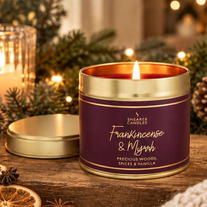 Shearer Frankincense and Myrrh large burgundy tin candle with gold lid beside evergreen branches and Christmas lights