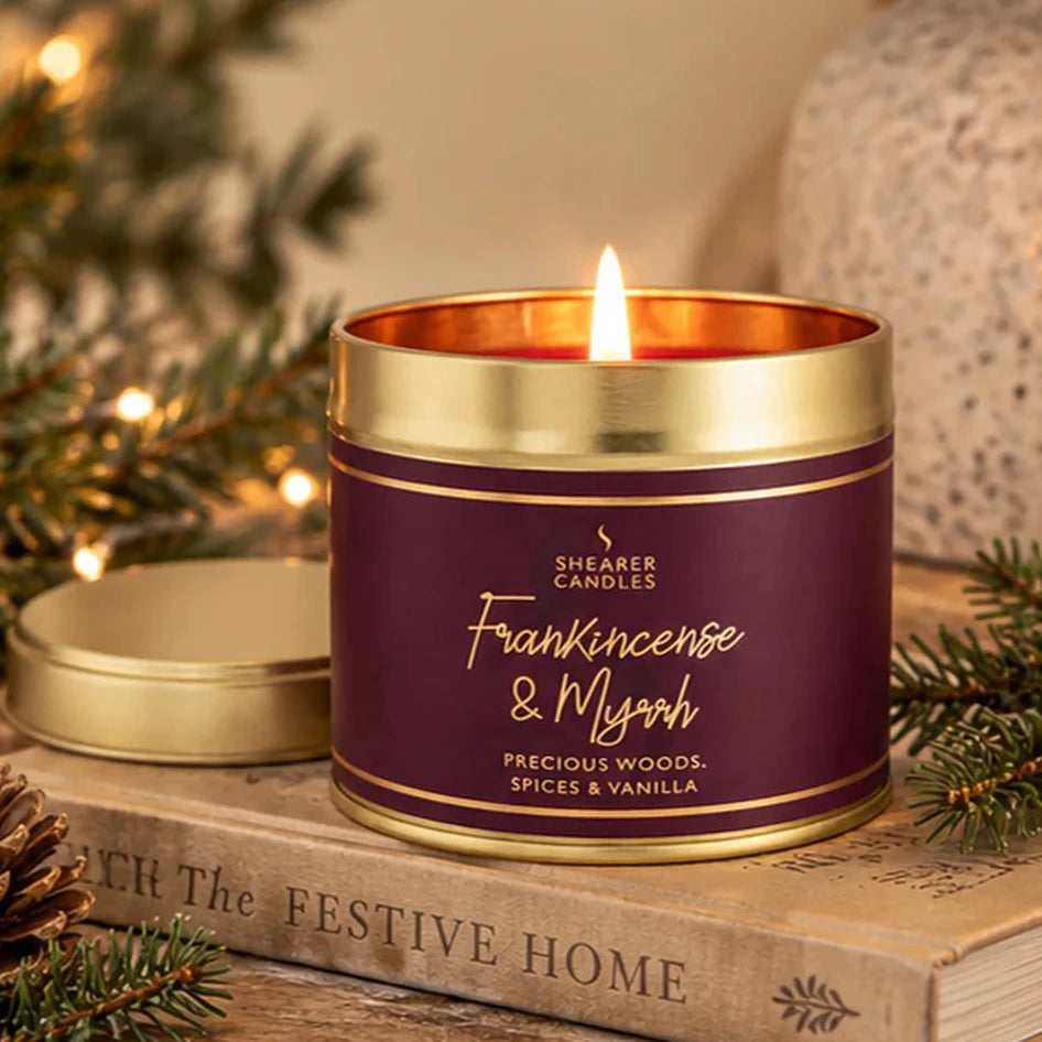 Large Frankincense and Myrrh candle in burgundy and gold tin styled with festive greenery and books