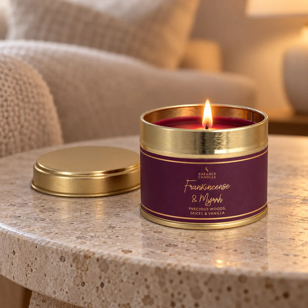 Frankincense and Myrrh small tin candle burning on a stone side table in a neutral living room.