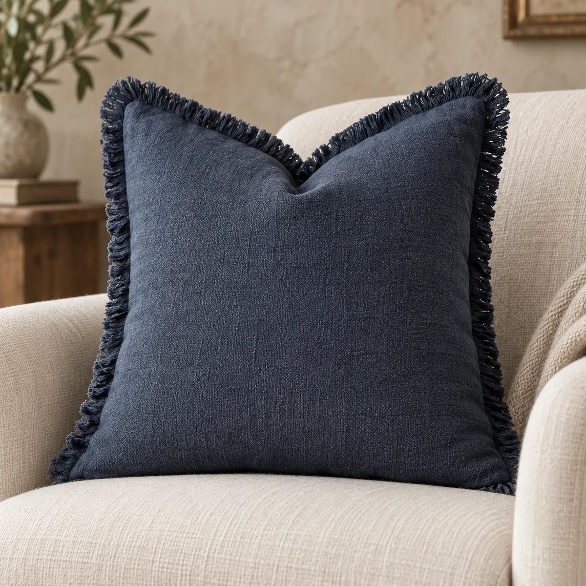 Navy blue cushion cover styled on a cream chair, with a close view of its textured fabric and frayed trim.