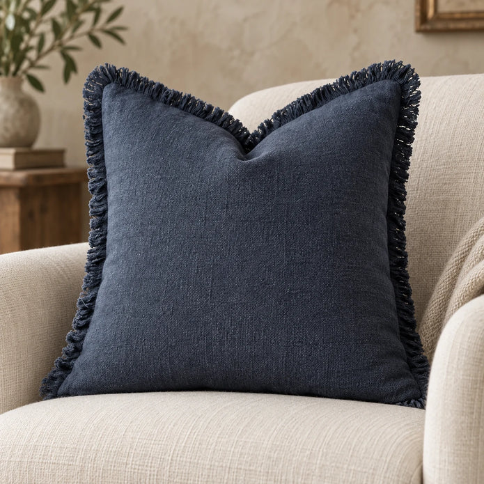 Navy blue cushion cover styled on a cream chair, with a close view of its textured fabric and frayed trim.