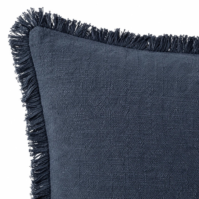 Close-up of a navy blue cushion corner showing the narrow frayed fringe and stitched edge on white.