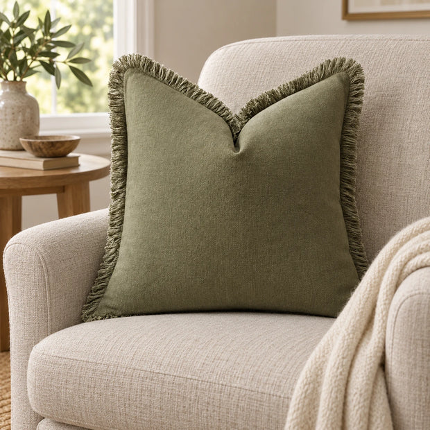 Frayed Edge Olive Green Cushion Cover styled on an upholstered reading chair in soft window light.