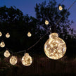 Galaxy Firefly warm-white festoon lights with glowing clear globe bulbs in a garden at dusk.