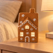Gingerbread glazed LED house with softly illuminated windows on a bedside table.
