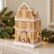 Gingerbread house with miniature trees styled on a stone mantel with greenery