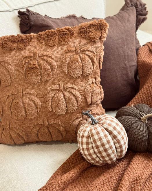 Decorative pillows with pumpkin pattern and small checkered pumpkin on a couch.