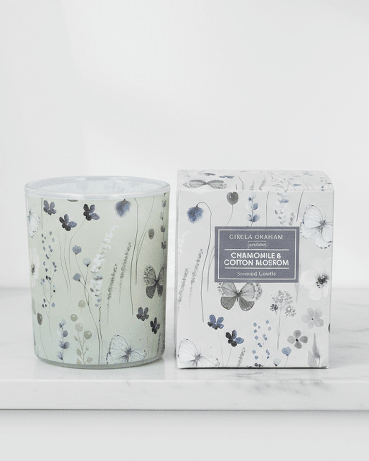 Gisela Graham chamomile and cotton blossom scented candle in a glass jar with a lit wick, showcasing a calming floral aroma.