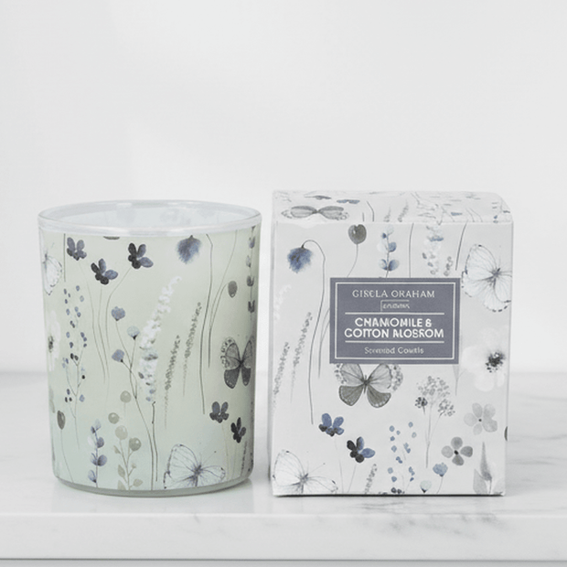 Gisela Graham chamomile and cotton blossom scented candle in a glass jar with a lit wick, showcasing a calming floral aroma.
