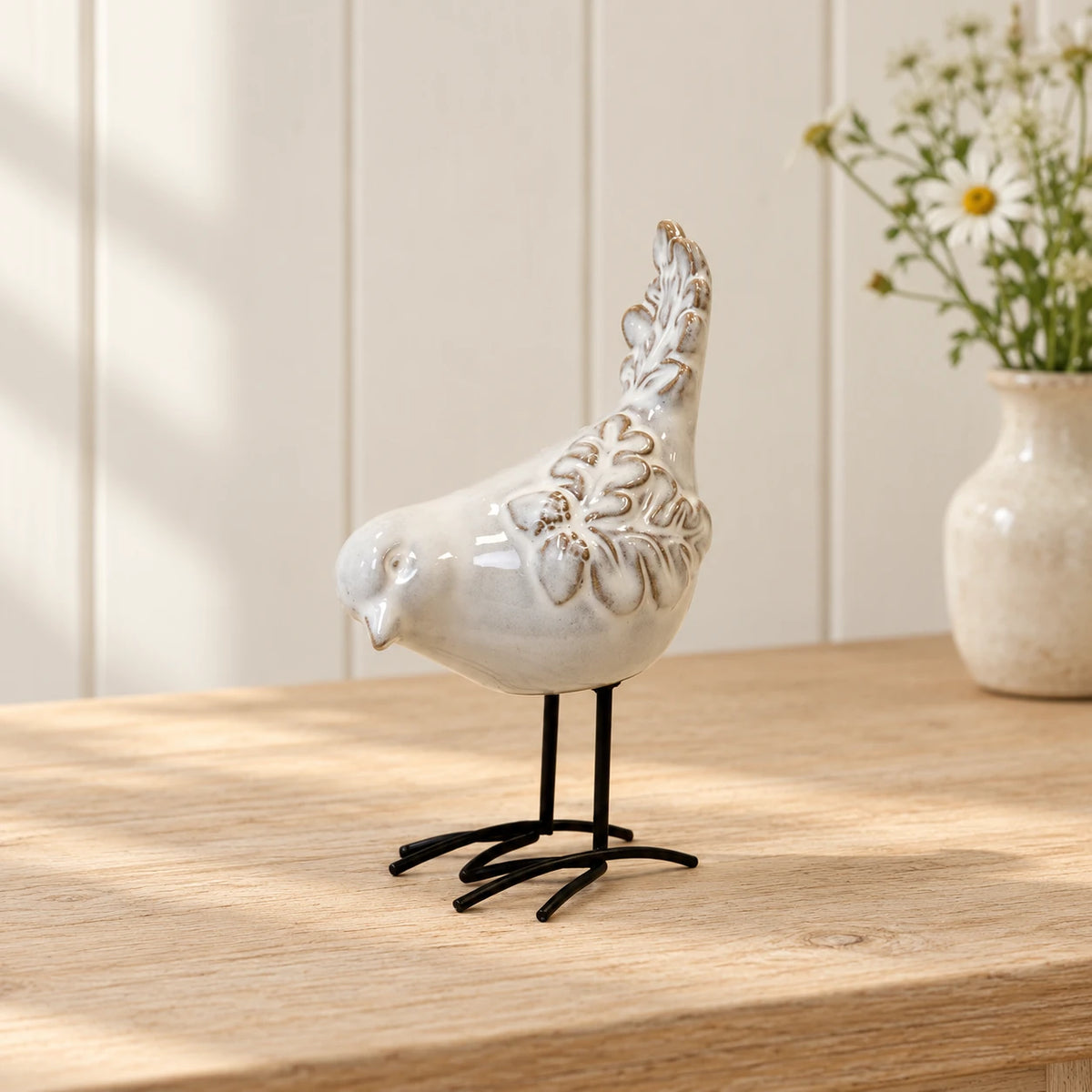 Glazed ceramic bird ornament with textured feathers and black metal feet on a light oak console