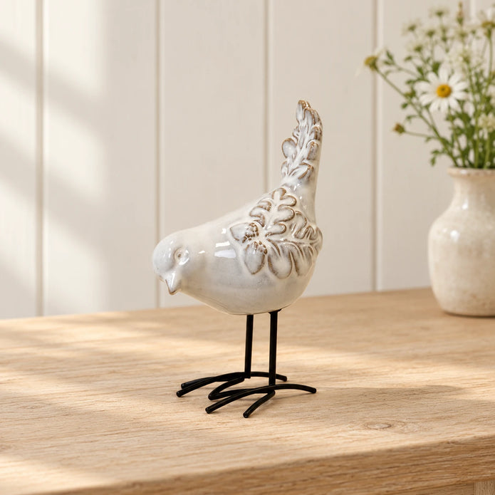 Glazed ceramic bird ornament with textured feathers and black metal feet on a light oak console