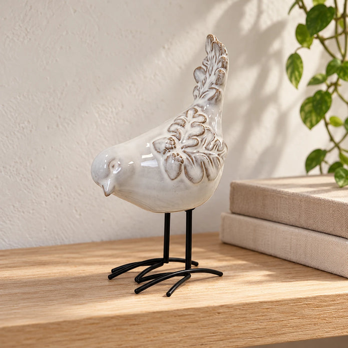 Ivory glazed ceramic bird ornament styled beside neutral books on a bright shelf
