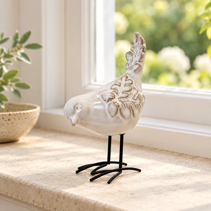 Small glazed ceramic bird ornament on a light stone windowsill with soft greenery beyond