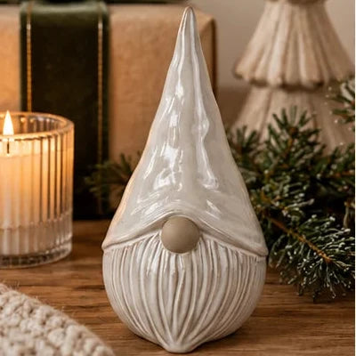 Neutral glazed ceramic gonk ornament beside candle and evergreen Christmas tree decoration