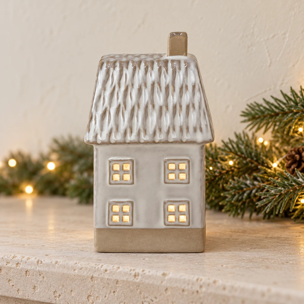 Illuminated ceramic house ornament on a limestone mantel with pine garland