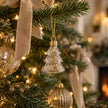 Gold glitter filled glass Christmas tree hanging from a fir branch with cream velvet ribbon