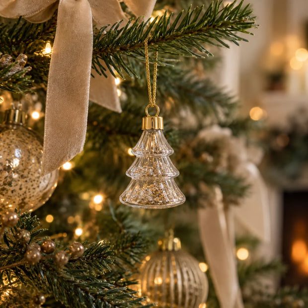 Gold glitter filled glass Christmas tree hanging from a fir branch with cream velvet ribbon
