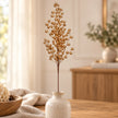 Gold Berries stem in a small cream vase on a wooden tabletop.