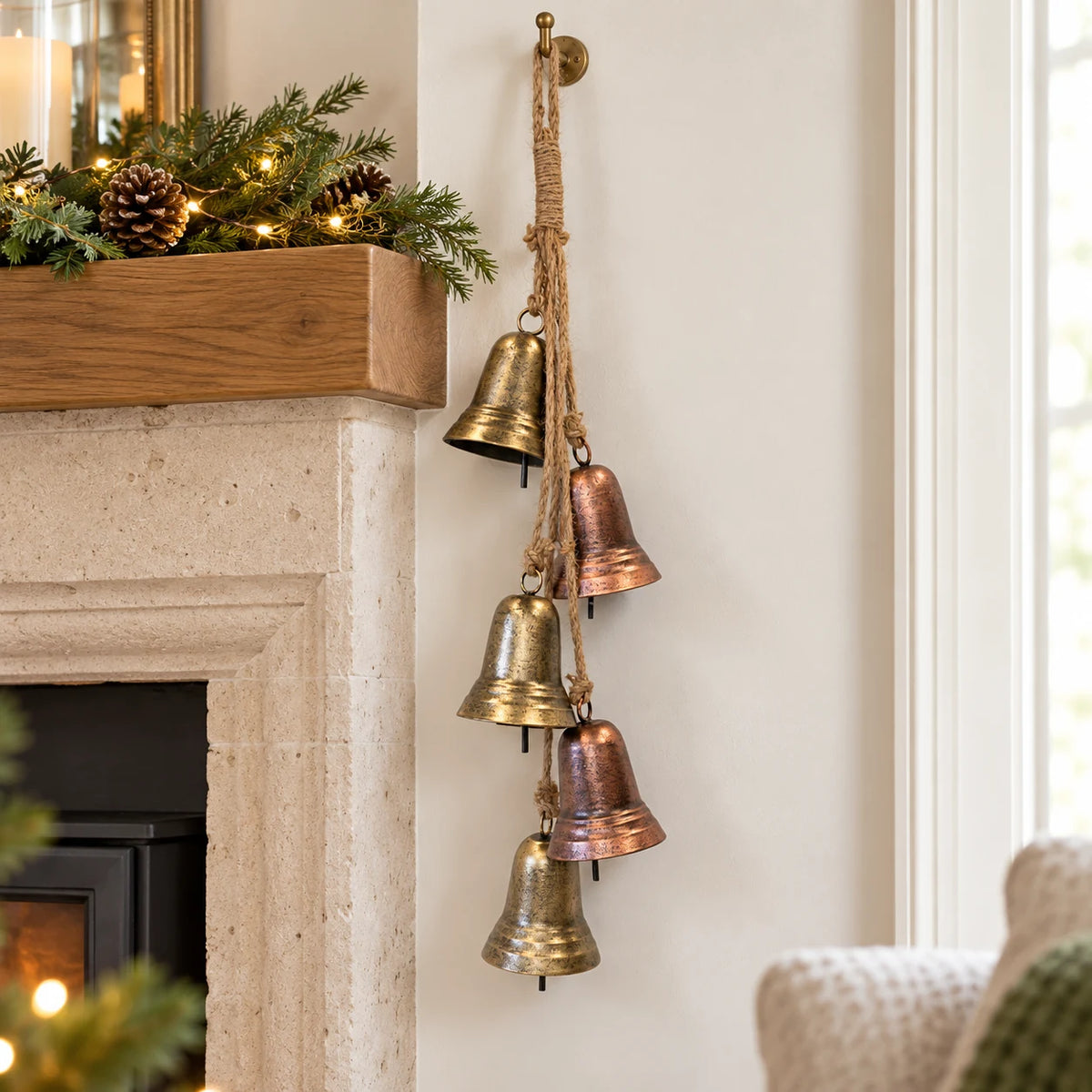 Five aged gold and copper bells hanging beside a pale stone fireplace at Christmas