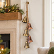 Five aged gold and copper bells hanging beside a pale stone fireplace at Christmas