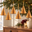 Six gold paper tree decorations hanging from fir branches above an oak sideboard.
