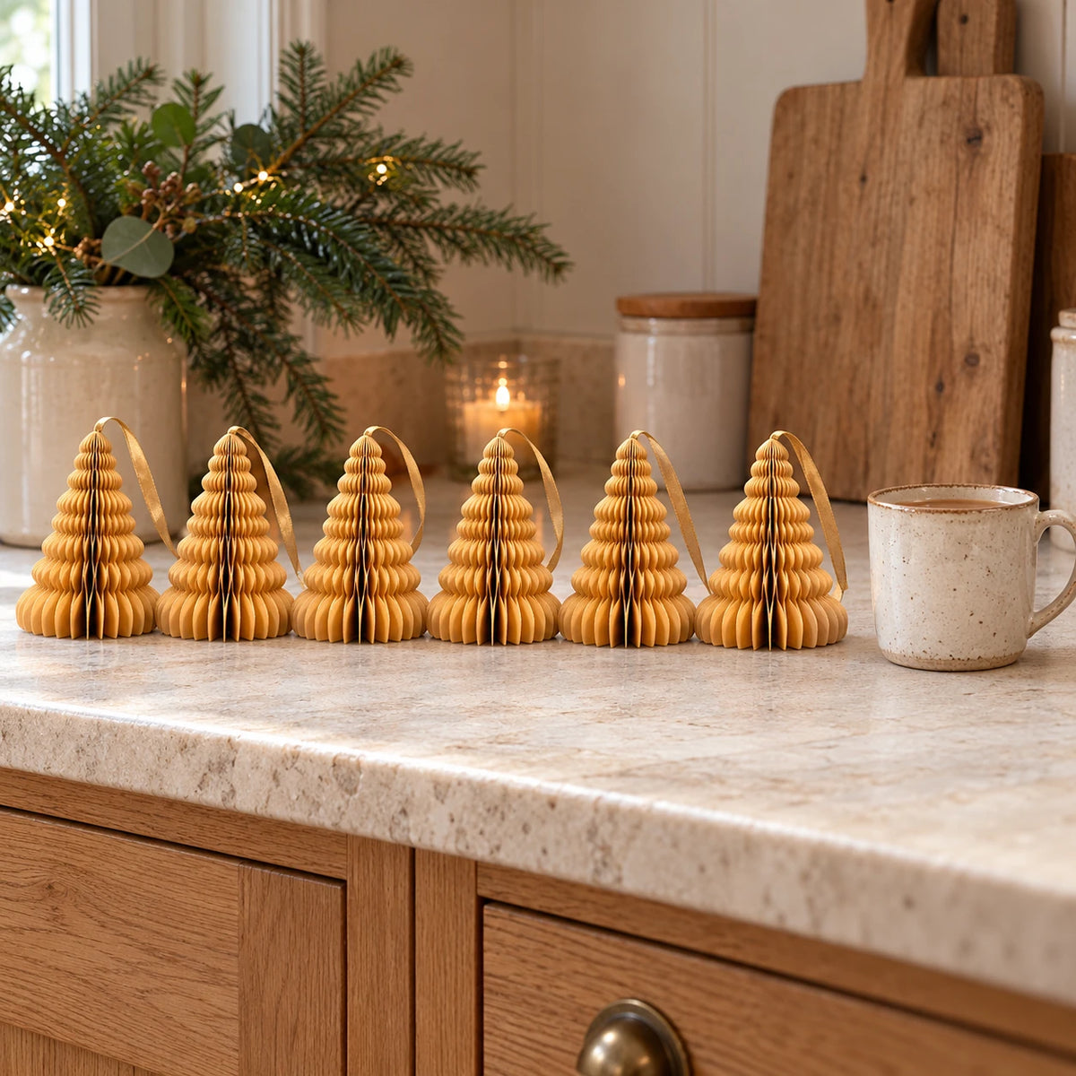 Six 11cm gold paper tree ornaments on a kitchen counter beside a mug of tea.