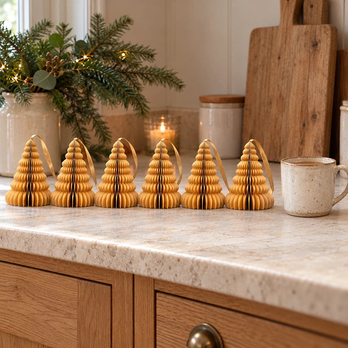 Six 11cm gold paper tree ornaments on a kitchen counter beside a mug of tea.