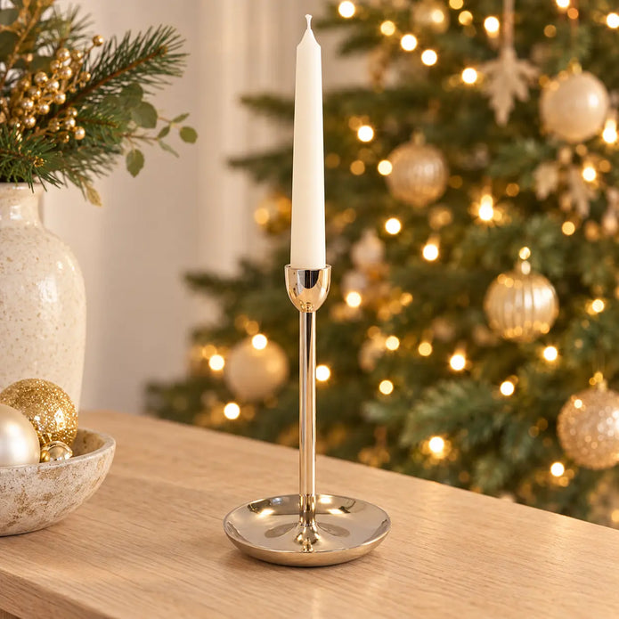 large gold metal candlestick holder with ivory candle on a Christmas console