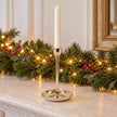 large gold metal candlestick holder with ivory candle on a festive mantel