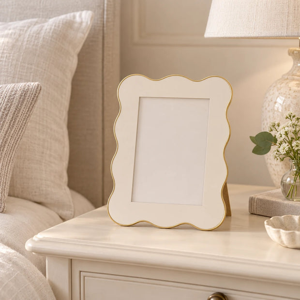 Small 4 x 6 inch ivory and gold scalloped photo frame on a cream bedside table.