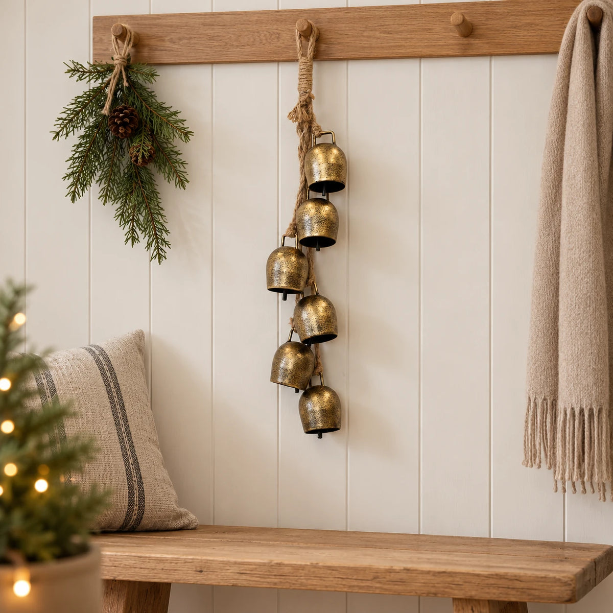 Six-bell gold hanging garland on an oak peg rail in a neutral Christmas hallway