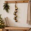 Six-bell gold hanging garland on an oak peg rail in a neutral Christmas hallway