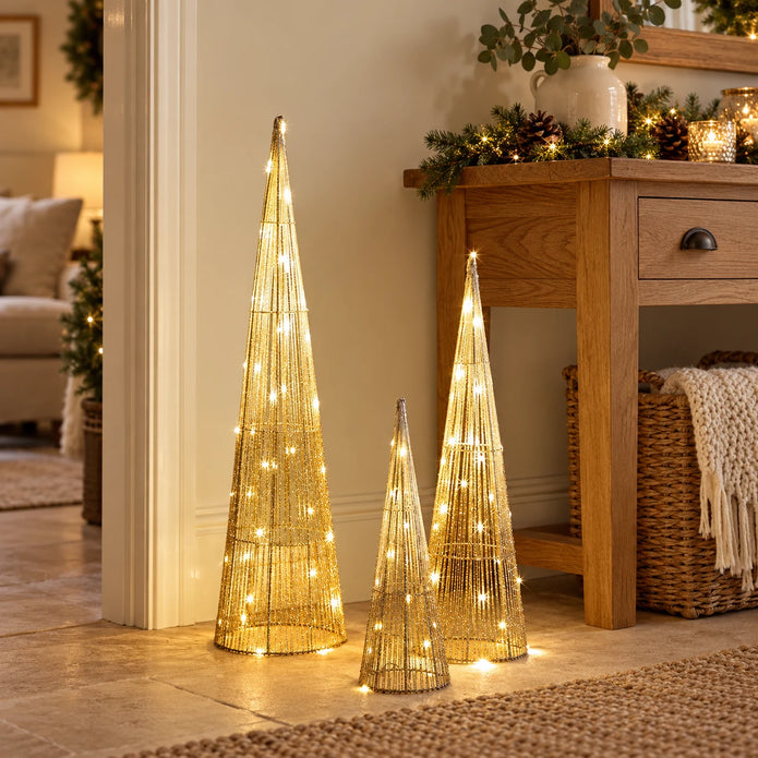 Three illuminated gold TreeBelisk cone trees beside an oak console in a neutral room.