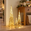 Three illuminated gold TreeBelisk cone trees beside an oak console in a neutral room.