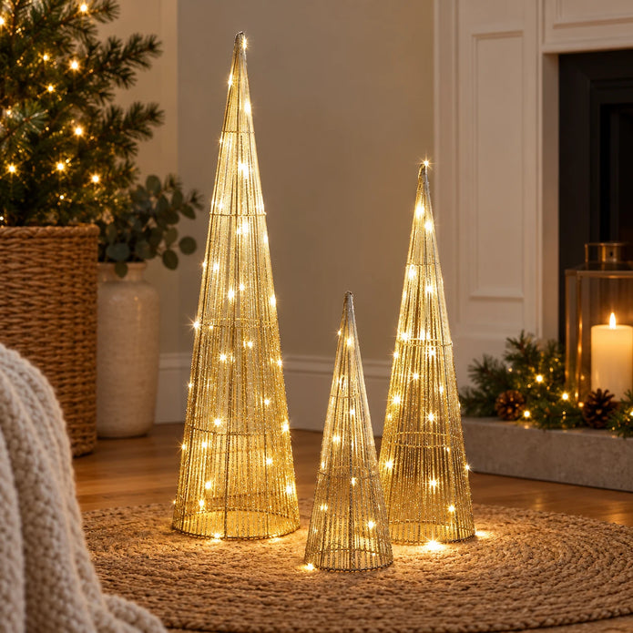 Gold TreeBelisk trees in three sizes glowing beside a Christmas tree and fireplace.