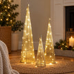 Gold TreeBelisk trees in three sizes glowing beside a Christmas tree and fireplace.