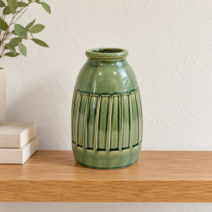 Medium green ceramic vase empty on an oak shelf with small neutral books well to the side.