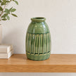 Medium green ceramic vase empty on an oak shelf with small neutral books well to the side.