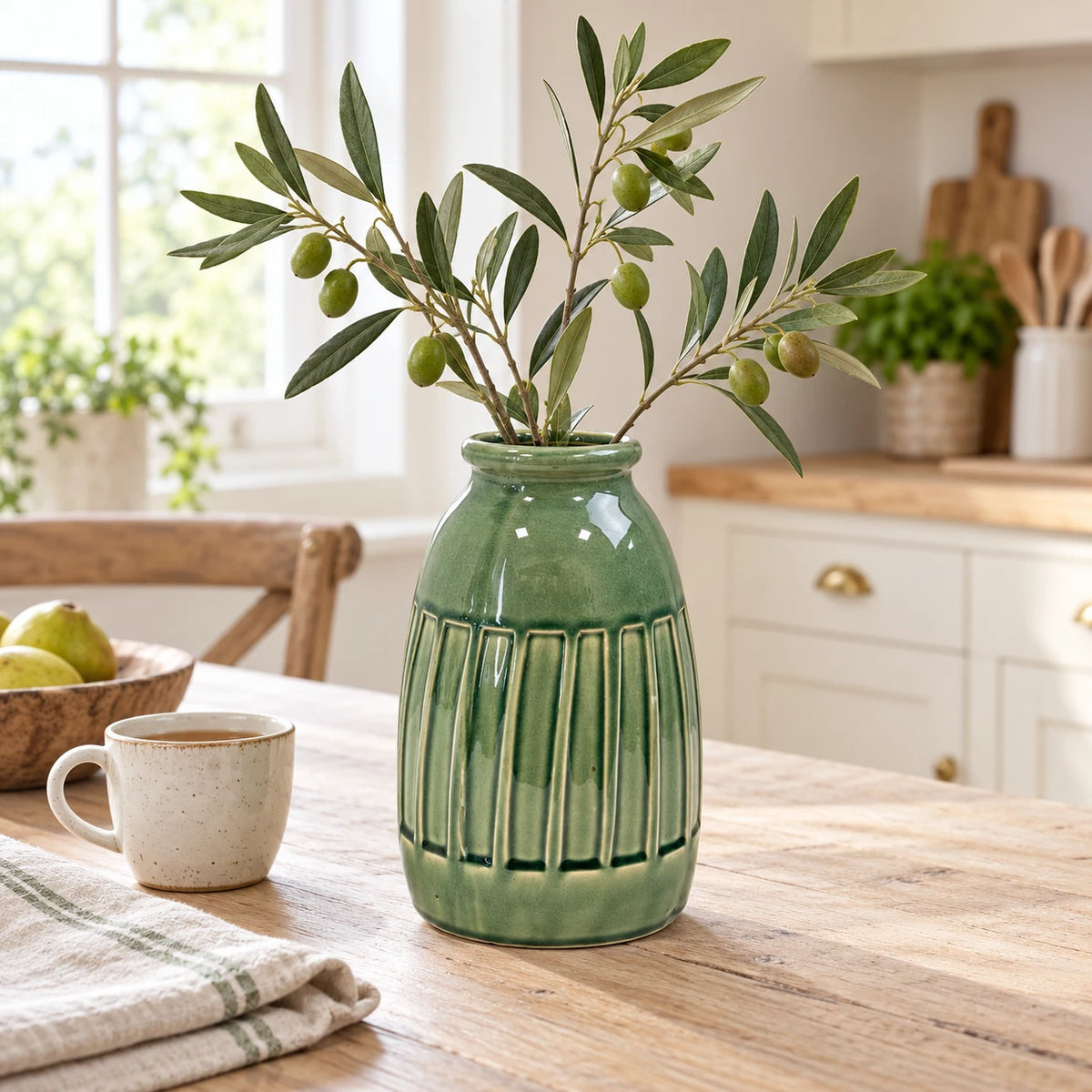 Medium green ceramic vase with three olive stems on a light kitchen table.