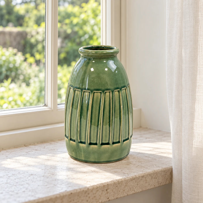 Medium green ceramic vase empty on a deep pale stone windowsill.