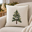 Green Christmas tree embroidered cushion cover styled on a cream boucle armchair with neutral Christmas decor.