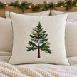 Cream cushion cover with an embroidered green tree and white snowflakes styled on ivory Christmas bedding.