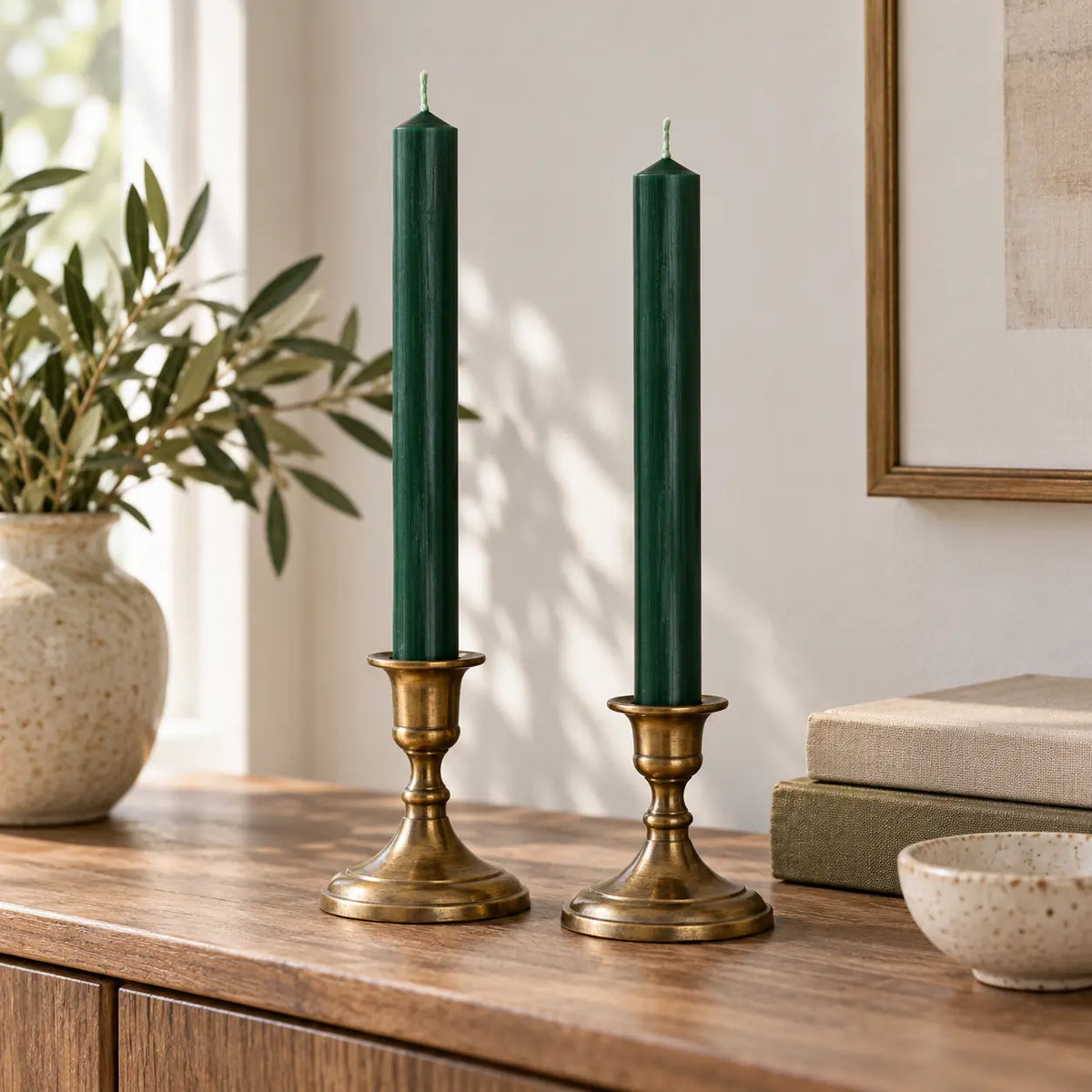 Pair of unlit green dinner candles in antique-brass holders on a neutral sideboard.