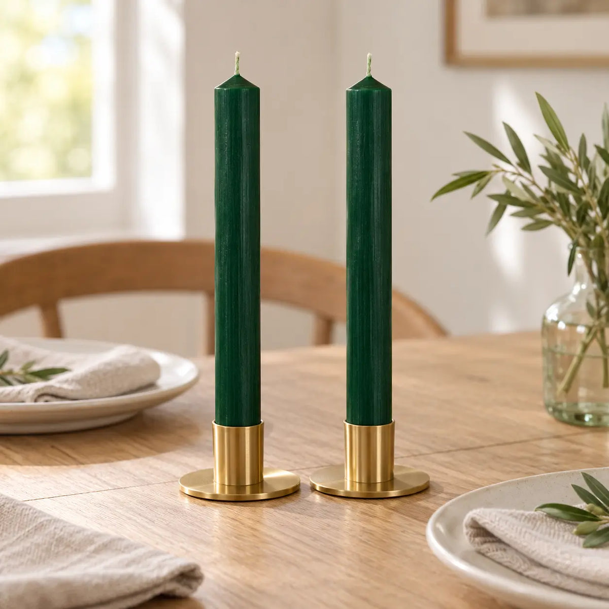 Pair of unlit green dinner candles in brass holders on an everyday dining table.